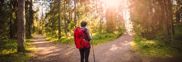 woman with red backpack standing at a forked path in the woods