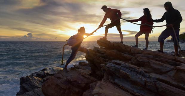 Friends help each other climb a rocky shore